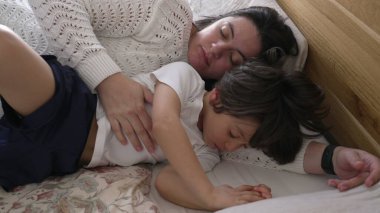 Anne ve çocuk yatakta huzur içinde uyuyor, huzurlu ve samimi bir dinlenme ve kaynaşma anı yakalıyorlar, paylaştıkları sevgi ve rahatlığı vurguluyorlar.