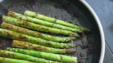 Buhar yükselen bir tavada taze kuşkonmaz pişirme, taze malzemelerin ve sağlıklı pişirme tekniklerinin kullanımını vurgulama, canlı rengi ve sebzenin besleyici değerini vurgulama,