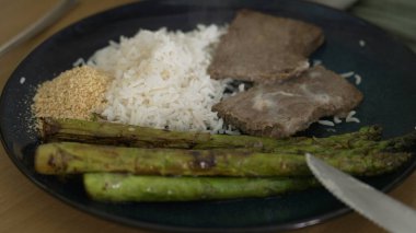 Izgara kuşkonmaz, buğulanmış beyaz pirinç, taze biftek ve ezilmiş sarımsak tabağı. Yemek fotoğrafçılığı ve mutfak sunumlarında dengeli ve besleyici bir yemek sergilemek için mükemmel.