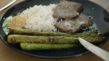 Izgara kuşkonmaz, buğulanmış beyaz pirinç, taze biftek ve ezilmiş sarımsak tabağı. Yemek fotoğrafçılığı ve mutfak sunumlarında dengeli ve besleyici bir yemek sergilemek için mükemmel.