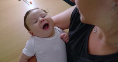 Bebeğin gülümsemesi, ebeveynlerinin kucağında yatarken, saf mutluluk ve neşe anlarını yakalıyor, çocukluk zamanlarının masumiyetini ve zevkini sevgi dolu bir evde gösteriyor.