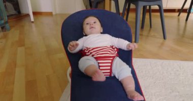 Bebek bir fedainin içinde uzanıyor, mutlu ve rahat görünüyor, rahat bir ev ortamında bir anlık rahatlığın tadını çıkarıyor, çocukluk yıllarının masumiyetini ve huzurunu vurguluyor.