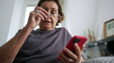 Üst düzey kadın elinde akıllı telefon cihazıyla içeriği okuyor, 70 'lerin yaşlı kadını okuma gözlüğü takıyor ve iletişim için telefon teknolojisini kullanıyor.