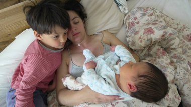 Aile zamanı - anne ve oğul yeni doğan bebeği yatakta dinlenirken takdir eder, yeni aile üyesini karşılarlar.