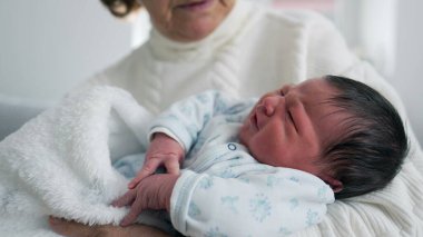 Büyükanne kucağında yeni doğmuş bir bebeği kucağında tutuyor, bebek ağlamaya başlıyor. Hayatın ilk günleri, ilk aşama