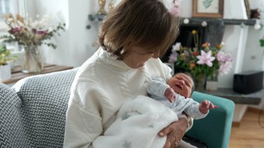 Büyükanne kucağında yeni doğmuş bir bebeği evdeki kanepede oturtuyor. Nesiller arası bağ arasındaki özgün aile anı. Büyük anne ve büyük baba ilk günlerinde bebeğe bakarlar.