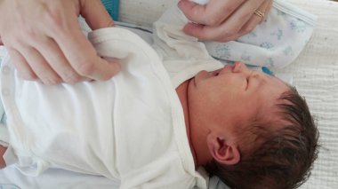 Anne, yeni doğanı giydiriyor. Anne, yeni doğan oğlunun ellerini nazikçe giydiriyor. İlk günlerdeki anne ve çocuk arasındaki sevgi dolu ilişkiyi anlatıyor.