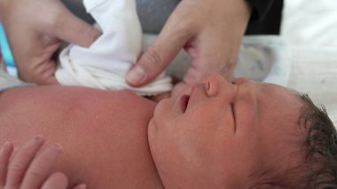 Hayatının ilk günlerinde yeni doğmuş bebeğe yakın çekim giydirmek. Annenin eli, oğlunun minik ellerine giysi koyuyor.