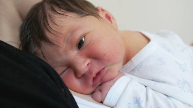 Yeni doğmuş bebek bebek, hayatının ilk haftasında yakın plan yüzü, annesinin kollarında dinlenen küçük sevimli bebek.