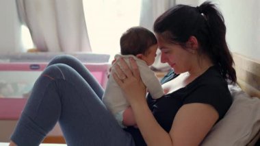 Anne ve bebek, alınları birbirine değerek, sıcak ve samimi bir ortamda sevgi ve bağ kurarak, yatakta hassas bir anı paylaşıyorlar.