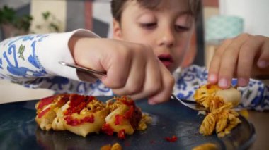 Dağınık saçlı genç bir çocuk ev yapımı enchilada 'lardan büyük bir ısırık alıyor, aile yemeği sırasında keyifle gülümsüyor.