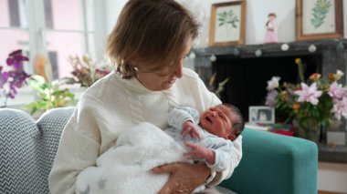 Yeni doğmuş bebeği kucağına aldığı için mutlu bir büyükanne. Oturma odasındaki koltukta oturup ağlayan bebekle ilk günlerinde iletişim kuruyor.