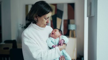 Büyükanne kucağında ve yeni doğmuş bebek torunu kollarında tutarken hayatın ilk günlerinde pencerede dikilirken, özgün aile bağı anı