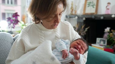 Yeni doğmuş bebeği kucağına aldığı için mutlu bir büyükanne. Oturma odasındaki koltukta oturup ağlayan bebekle ilk günlerinde iletişim kuruyor.