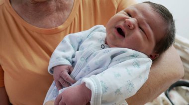 Büyükanne kucağında yeni doğmuş bir torun taşıyor. Hayatın ilk günlerinde doğan bebek, farklı nesillerin bir arada olması gibi.