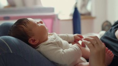 Annenin bacağından tutulan yeni doğmuş bir bebeğin yüzü, yumuşak ve rahat bir çevreyle çevrili bebeğin masumiyetini ve sükunetini yakalıyor.