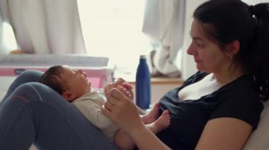 Anne ve yeni doğmuş bebek bir yatakta etkileşime giriyor, birbirlerine sevgi ve sevgiyle bakıyor, sıcak bir ortamda hassas ve samimi bir aile anı yaratıyor.