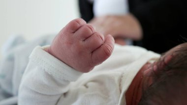 Yaşamın ilk günlerinde küçücük bir bebeğin elleri. Anne onu bulanık bir arka plan ile giydirirken yeni doğmuş bir bebeğin el işi.
