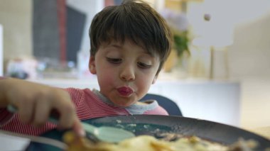 Yemek saatinde yemek yiyen küçük çocuk, 5 yaşındaki çocuğun yakın çekimi kaşıkla ezilmiş patatesler yiyen, yuvarlanan gözler ve akşam yemeği saatinde aptalca davranan çocuk.