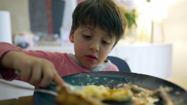 Küçük çocuk çatalla patates eziyor, çocuk yemek saatinde tabakta yemek yiyor, yemek yiyen çocuğun yakın plan yüzü.