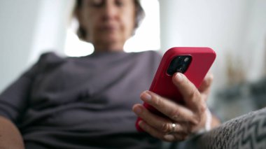Ev koltuğunda oturan üst düzey bir kadının cep telefonu cihazının yakın çekimi, içeriği internetten okuyan kişi, teknoloji telefonu.