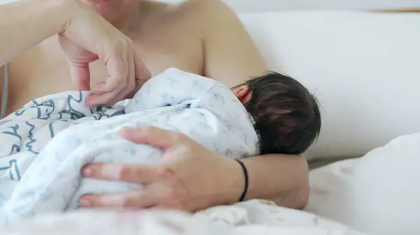 stock image Mother caresses newborn baby's head while breastfeeding, mom bonding with her infant baby during first days of life laid in bed