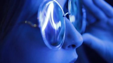 Geceleyin neon ışığı yansıması ile büyük yuvarlak güneş gözlüğü takan kız.