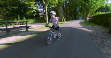 Bisikletle ağaçlık bir patikadan aşağı inen, güvenlik için kask takan, yeşil ve doğa ile çevrili, aktif bir günün tadını çıkaran genç çocuk.