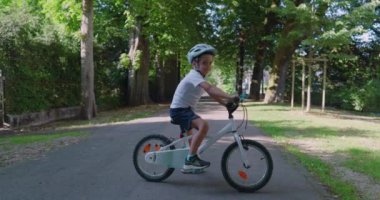 Parkta bisikletli gülümseyen bir çocuk, güvenlik için kask takıyor, ağaçlarla dolu bir yolda duruyor, güneşli bir günün tadını çıkarıyor, gençlik enerjisini sergiliyor.