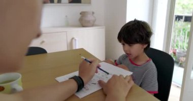 Genç bir çocuk, eğitim seansı sırasında eğitici materyallere odaklanmıştı. Annesi ona ahşap bir masada rehberlik ediyordu.