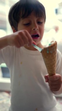 Dondurmanın tadını çıkaran genç bir çocuk, kaşıkla koniden zevk alıyor, basit ve keyifli bir çocukluk anını içeride yakalıyor.