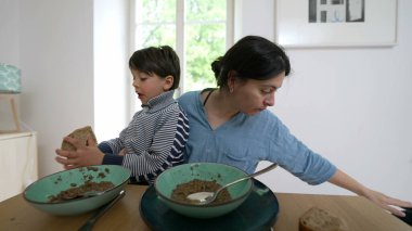 Anne, küçük oğlunu besleyerek ve yemek masasında yemeğini yiyerek birden fazla iş yapıyor. Aile bağı kurma anı ve yemek saatinde çocuğa bakma alışkanlığı