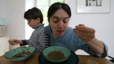 Anne, küçük oğlunu besleyerek ve yemek masasında yemeğini yiyerek birden fazla iş yapıyor. Aile bağı kurma anı ve yemek saatinde çocuğa bakma alışkanlığı