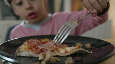 Bir çocuğun pizza yemek için çatal kullanması, dilime ve çocuğun eline odaklanması, yemek zamanı nişan anı yakalaması ve yemeğin keyfini çıkarması.