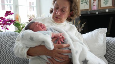 Büyükanne sevgiyle kucağında yeni doğmuş bir bebek, hassas aile bağları, huzurlu bir ev içi, nesiller arası bağ, büyükannenin bakımı ve sevgisi