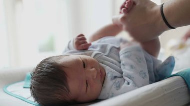 Yeni doğan bebek masa değiştiriyor, annesinin ellerindeyken yukarı bakıyor, bir evde rutin bebek bezi değiştirme sırasında etkileşimi ve bağı yakalıyor.