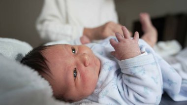 Yeni doğan bebek yukarı bakarken, büyükanne bebek bezi değişiminden sonra kıyafet giyer, hassas ve şefkatli bir an, aile bağları, sıcak ev ortamı, çok nesilli aşk