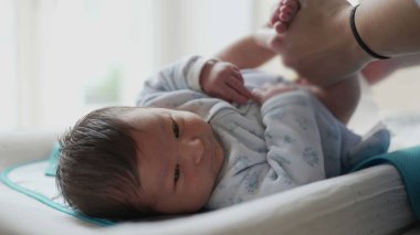 Yeni doğan bebek masa değiştiriyor, annesinin ellerindeyken yukarı bakıyor, bir evde rutin bebek bezi değiştirme sırasında etkileşimi ve bağı yakalıyor.
