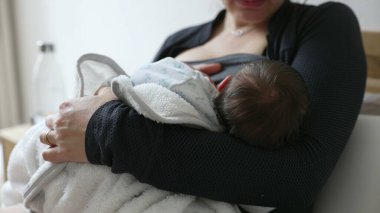 Anne yeni doğmuş bebeği emziriyor, yumuşak bir battaniyeye sarılıp anne ve çocuk arasındaki yakın ve besleyici bir annelik anını yakalıyor.