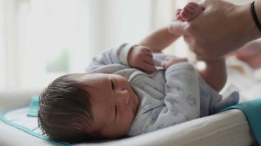Yeni doğan bebek masa değiştiriyor, annesinin ellerindeyken yukarı bakıyor, bir evde rutin bebek bezi değiştirme sırasında etkileşimi ve bağı yakalıyor.