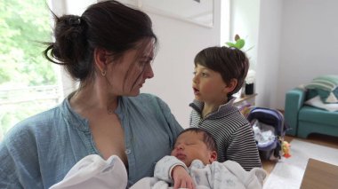 Anne ve küçük oğul yeni doğmuş bebeği tutarken etkileşime girerler. Yürekten bir aile anını yakalarlar. Samimi ve sevgi dolu bir aile sahnesi.