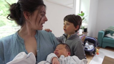 Anne ve küçük oğul yeni doğmuş bebeği tutarken etkileşime girerler. Yürekten bir aile anını yakalarlar. Samimi ve sevgi dolu bir aile sahnesi.