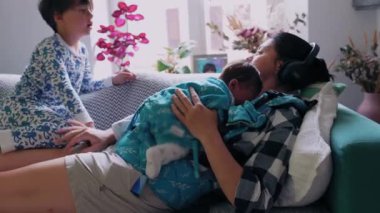 Anne, yeni doğmuş bebeğini büyük kardeşiyle evdeki kanepede emziriyor. 