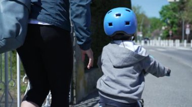Küçük çocuk güneşli bir günde annesiyle dışarıda koruyucu kaskla bisiklet sürüyor.