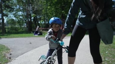 Küçük çocuk güneşli bir günde annesiyle dışarıda koruyucu kaskla bisiklet sürüyor.
