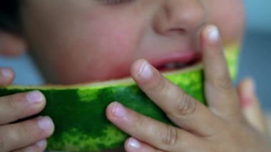Çocuk bir dilim karpuzun tadını çıkarıyor, açık ve güneşli bir ortamda ferahlatıcı bir yaz meyvesi yemenin sevincini ve neşesini gösteriyor.