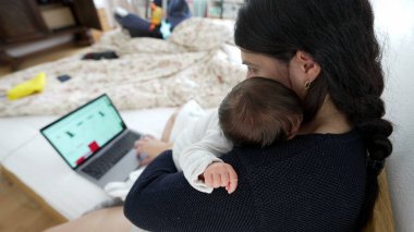 Anne kucağında yeni doğmuş bir bebek varken dizüstü bilgisayarda çalışıyor, mesleki görevlerin ve ebeveynlik sorumluluklarının dengesini gösteriyor, modern aile yaşamını ve çoklu görev becerilerini vurguluyor