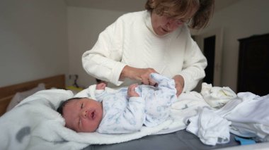 Büyükannem yeni doğan bebeklere beyaz tulum giydirir. Bebek yumuşak bir battaniyeye uzanır, ağzı şaşkınlıkla açılır, erken yaşlarda kuşak bağının ve şefkatin yürek ısıtan anını yakalar.