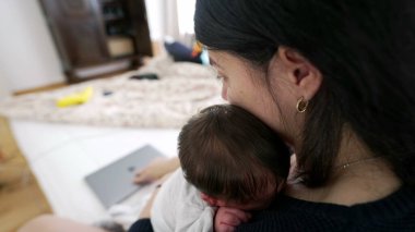 Anne, tamamen yeni doğmuş bebeğine odaklanmak için dizüstü bilgisayarını kapatıyor. Aile bakımını işe tercih ettiği hassas bir an. Modern anneliğin duygusal bağını ve adanmışlığını vurguluyor.