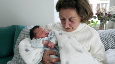 Yaşlı bir kadın sevgiyle yeni doğmuş bebeği bir battaniyeye sardı, hassas aile bağları, büyükannenin bakımı, huzurlu ev ortamı, nesiller arası bağ.